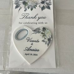 a white heart shaped keychain with flowers on it and the words thank you for celebrating with us