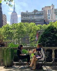 two women sitting in lawn chairs talking to each other on a sunny day with skyscrapers in the background