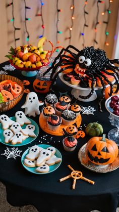 a table topped with lots of halloween treats and desserts next to a spider on top of a black table cloth