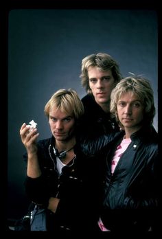 three young men are posing for a photo in front of a black background and one is holding an object