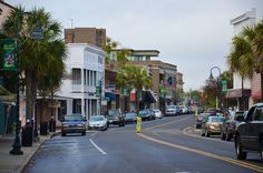 cars are parked on the street in front of buildings and palm tree's lining the sidewalk