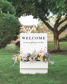 a welcome sign sitting in the middle of a field with flowers and greenery on it