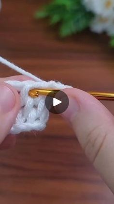 someone crocheting the end of a piece of white yarn with a golden needle