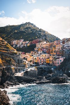 an ocean view with houses on the hillside and blue water in the foreground, surrounded by rocky cliffs