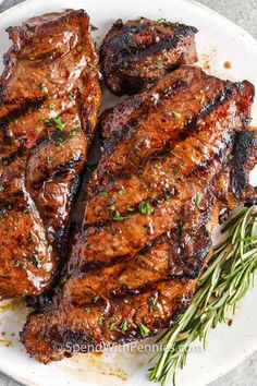 grilled steaks on a white plate with rosemary garnish