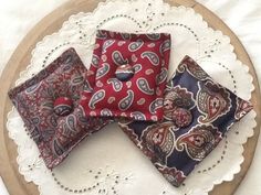 three red and blue paisley pocket squares on a white doily with lace trim around the edges