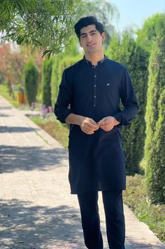 a man standing in front of a tree wearing a black shirt and pants with his hands together