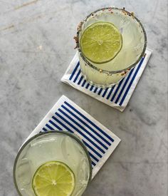 two glasses filled with lemonade and lime slices on top of striped napkins next to each other