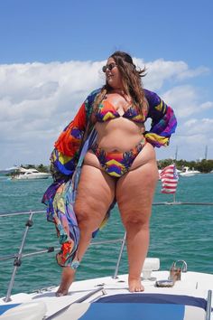 A woman on a sunny boat ride poses in a vibrant bikini and long, colorful cover-up. The bright sky, sparkling green water, and distant shoreline create a tropical, carefree atmosphere.