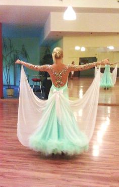 a woman in a green and white dress standing on a hard wood floor with her arms outstretched