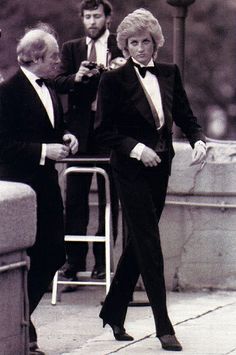 two men in tuxedos are walking down the street with another man standing next to them