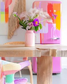 a pink vase filled with flowers sitting on top of a wooden table next to a chair