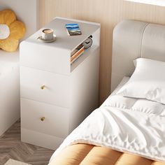 a white nightstand next to a bed with pillows and a cup of coffee on it