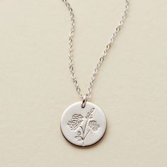 a necklace with a flower engraved on the front and back, hanging from a silver ball chain