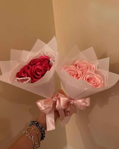 two roses are being held up by someone's hand with pink bows on them