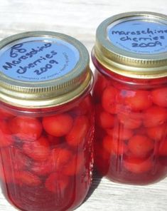 two jars filled with red tomatoes sitting on top of a wooden table next to each other