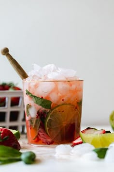 a glass filled with fruit and ice next to sliced limes, strawberries and lime wedges