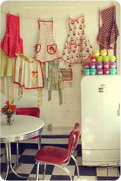 there are many aprons hanging on the wall next to a table with chairs and a refrigerator