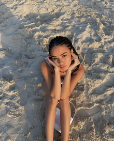 a woman laying in the sand with her hand on her head and looking at the camera