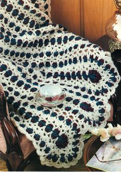 a crocheted blanket sitting on top of a chair next to a vase with flowers