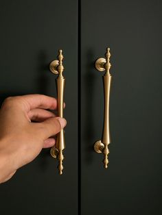 a hand is holding the handles to a black door with gold hardware and knobs