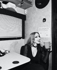 a woman sitting at a table drinking from a cup