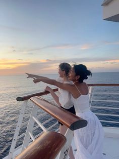 two women standing on the deck of a boat pointing at the sunset over the ocean