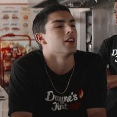 two young men sitting at a table in a restaurant, one is talking to the other