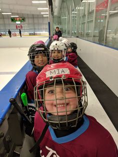 three young children wearing helmets on an ice rink