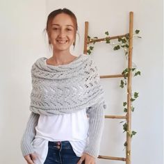 a woman standing in front of a ladder wearing a knitted shawl and jeans