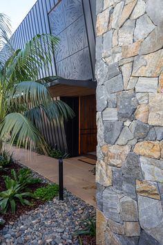 the entrance to a modern house with stone walls and plants on either side of it