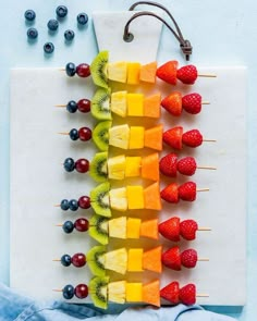 fruit skewers are arranged on a cutting board with berries and kiwis