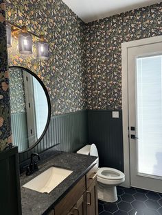 a bathroom with floral wallpaper and black tile flooring, along with a white toilet