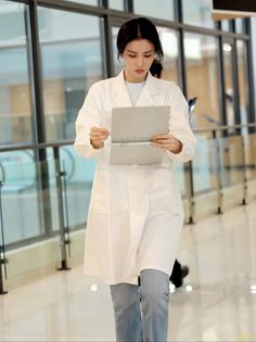 a woman in a white lab coat is looking at something on her lap top while walking through an airport