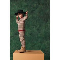 a young boy in striped pajamas and hat standing on top of a cardboard box with his hand up