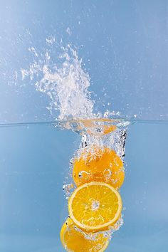 three oranges falling into the water with splashing from above and below, on a blue background