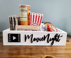 a movie night sign with popcorn, soda and snacks in it on a wooden table