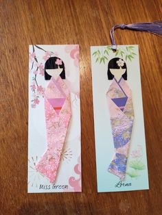 two bookmarks made out of paper on top of a wooden table