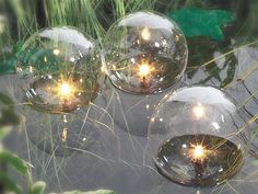 three clear glass balls with lights in them sitting on the ground next to some grass