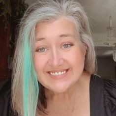 a woman with long grey hair and blue eyes smiles at the camera while wearing a black top