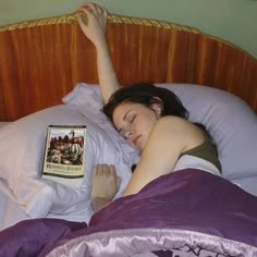 a woman laying in bed reading a book with her hand on top of the pillow