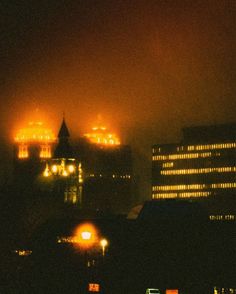 the city skyline is lit up at night, with lights shining in the foggy sky