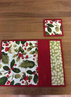 two placemats with red and green designs on them sitting on a wooden table