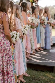 a group of women standing next to each other in front of a wooden bench holding bouquets