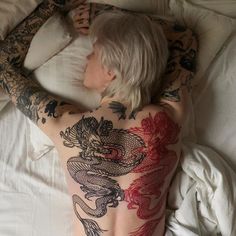 a tattooed man laying in bed with his back turned to the side and arms behind him