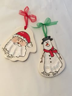 two ceramic ornaments with santa claus and snowman on them, hanging from red ribbon