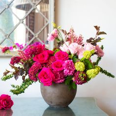 a vase filled with pink and green flowers sitting on top of a table next to a mirror