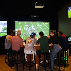 four people sitting at a bar playing video games on the big screen tv's