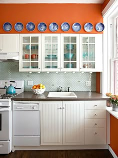 a kitchen with white cabinets and blue plates on the wall above the sink, along with orange walls