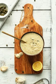 a wooden cutting board topped with a bowl of soup next to garlic and an orange